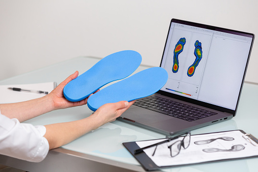 Female doctor orthopedist  holding custom made insoles in a clinic in front of the laptop with a test feet picture.  Feet recreation and orthotic medicine concept. Feet recreation medicine concept