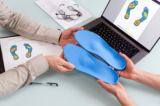 Female doctor orthopedist  presents new custom made insoles to a male patient in a clinic.   Feet recreation and orthotic medicine concept