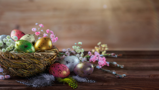 Easter eggs in a nest and small beautiful flowers behind a nest on empty rustic wooden table with defocused sunlight at background. Easter composition with copy space. Spring backdrop with bokeh for product display on top of the table.