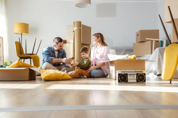 Happy young family unpacking belongings from boxes in new apartment Happy family with one child starting new life in new apartment. They are unpacking boxes and talking to the child while sitting on the floor home ownership stock pictures, royalty-free photos & images
