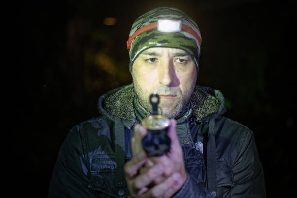 Close-up photo of a traveling man looking at compass in his hand at night. A man uses a headlamp to light the path and check his compass during his nighttime hiking adventure.