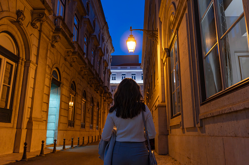 Rear view of woman walking on illuminated street at night