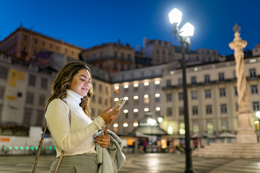 Mature woman using smartphone at dusk in the city center in Lisbon, Portugal