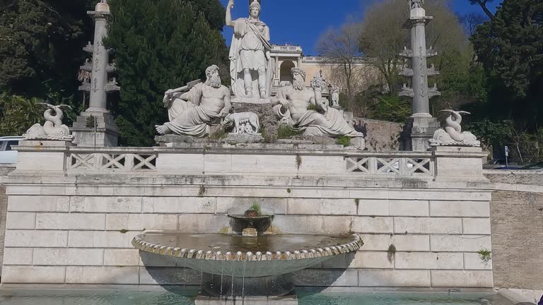 Aerial slow motion view of tourist people sitting relaxed at fountain with sculpture on Piazza del Popolo in Roma, Italy