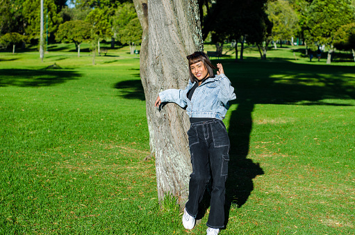 portrait of young woman with bobbed hair dressing casual clothes next to a tree in public park on a sunny day