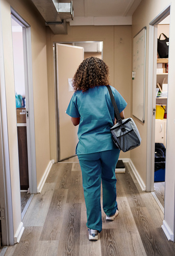 Rear view of a female doctor wearing scrubs walking with a bag along a corridor in a medical clinic