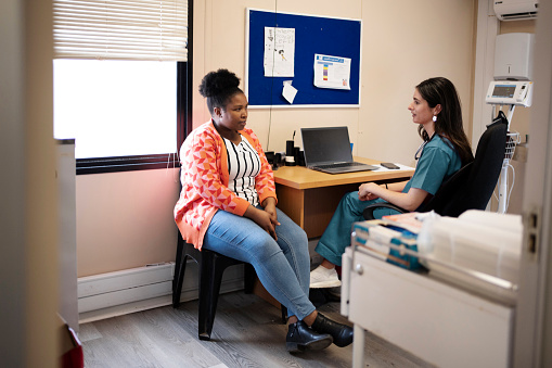 Female doctor wearing scrubs talking with a patient at a desk in her office during an appointment in a hospital