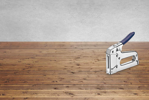 Heavy-duty chrome manual staple gun on a wood countertop background