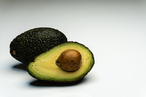 In this captivating image, a luscious avocado takes center stage, showcasing its unique and velvety texture. The fruit's dark green, pebbled skin contrasts with the creamy, buttery flesh revealed as it's halved. The rich, earthy tones of the avocado create a visually pleasing composition, while the subtle play of light accentuates its natural contours. The juxtaposition of the smooth seed against the creamy green flesh adds an element of visual interest. This photograph captures the essence of the avocado, a versatile and nutrient-rich fruit, inviting the viewer to appreciate both its visual appeal and the promise of a delicious and healthy culinary experience.