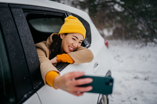 Young woman making a selfie through the car window on a snowy day