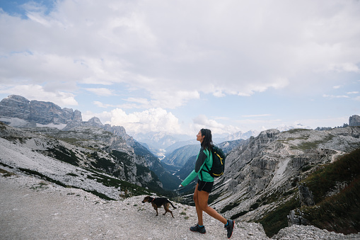 Female hiker enjoys the beautiful outdoors with her dog, walking on top of the Tre Cime di Lavaredo.