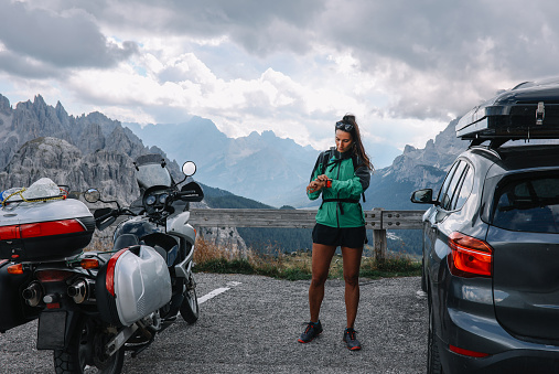 Female tourist enjoys the beautiful outdoors, arriving to the Italian Alps by a car or a motorcycle.