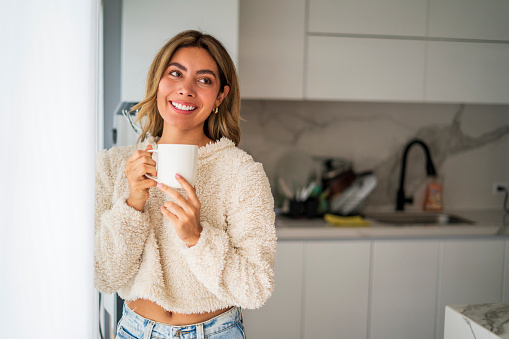 Latin woman aged between 25-35 years old is drinking coffee at home