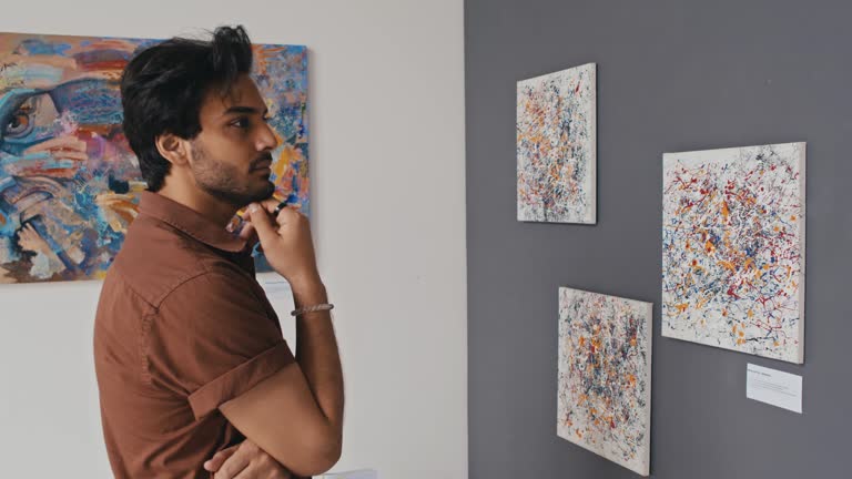 Young Male Visitor Looking at Abstract Paintings in Museum