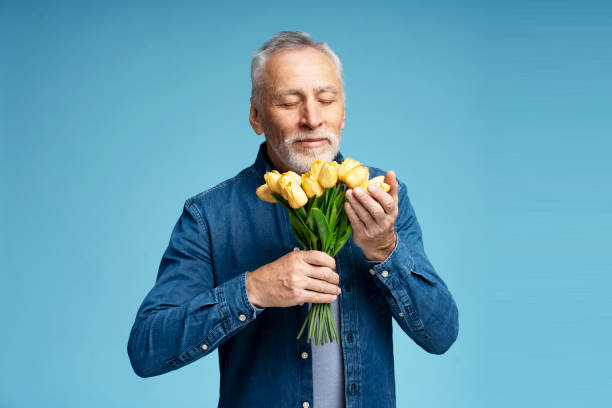 улыбающийся красивый пожилой мужчина в стильной джинсовой рубашке, держащий букет цветов, желтые тюльпаны - tulip blue close up cut flowers стоковые фото и изображения