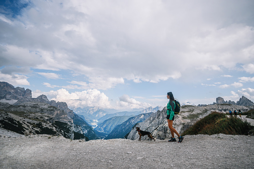 Female hiker enjoys the beautiful outdoors with her dog, walking on top of the Tre Cime di Lavaredo.