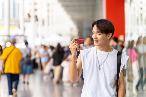 Portrait of Young Asian man holding credit card standing in front of shopping mall in the city. Generation z people enjoy shopping with contactless payment.