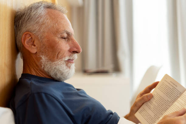 istock Closeup, handsome, serious senior man reading book, lying in bed, morning routine 1958605465