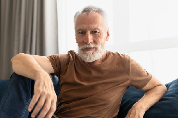 istock Attractive elderly man smiling sitting on soft sofa in living room and looking at camera 1958606017