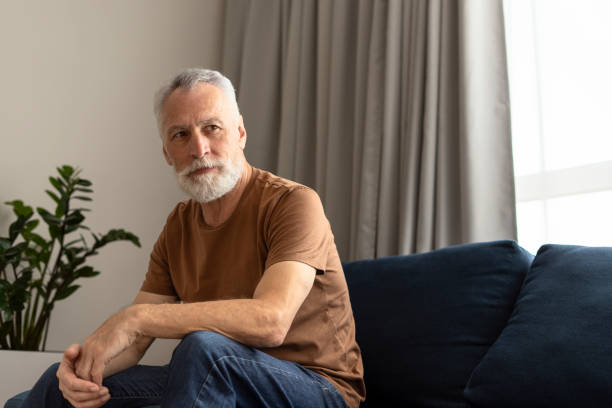 istock Lonely gray haired senior man looking away sitting on sofa in nursing home 1958606023