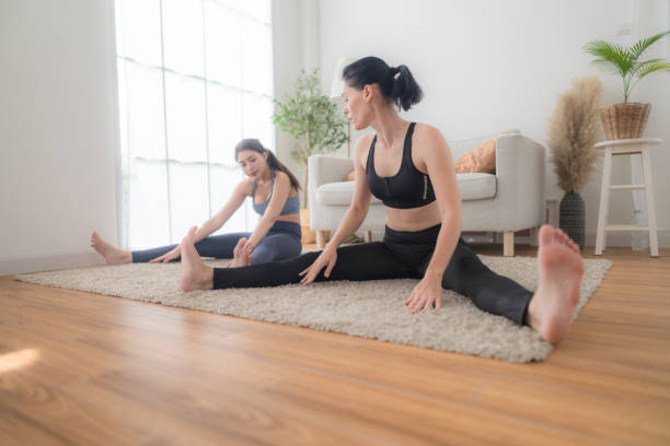 two women confident training yoga. athletic women in sportswear doing fitness stretching exercises at home in the living room. sport and recreation concept. yoga teacher is helping young woman. - yoga business women living room ストックフォトと画像