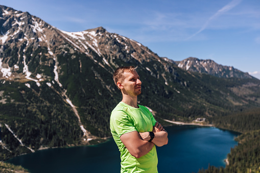 Male portrait of man, who traveling in mountains. Person doing hiking with green sportswear outdoors. Lifestyle photography of real people, tourism concept with smart watch.