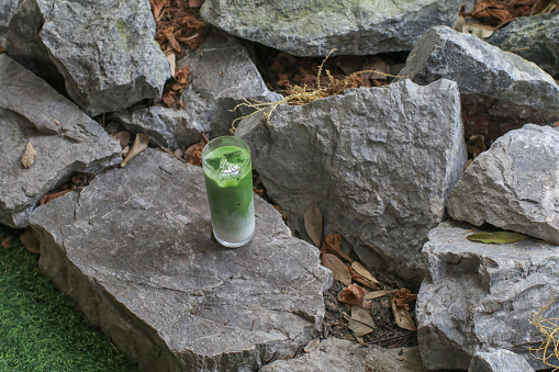 Iced Matcha green Tea latte on the rock with nature background. healthy Japanese drinks. Cold summer drink.