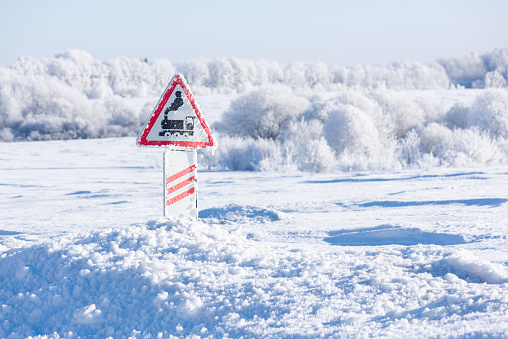Railway crossing sign, snowdrifts and snow-covered trees in frost on the background landscape