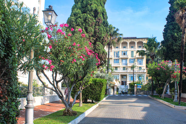 Corso Italia in Bordighera is one of the most elegant boulevard connecting the railway station in the lower town by the sea and the impressive hospital building (seen in the background) on the hill on via Romana. Bordighera in the Italian Province Liguria, Region Imperia, is a medieval town from the XV. century, also known as Regina delle Palme, The Queen of the Palm Trees. It is located on the Italian Riviera between the French border and Sanremo. Also called Riviera dei Fiori.