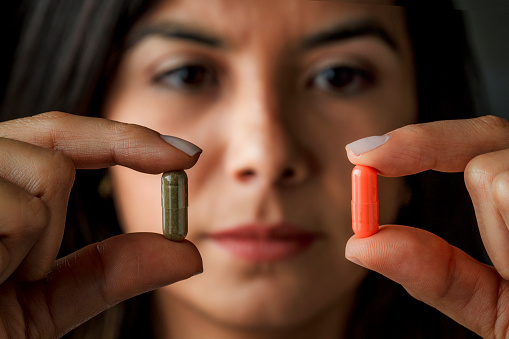 Health themes: Young Hispanic woman choosing between antibiotics or alternative medicine. Holding capsule with fingers.