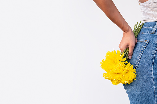 Anonymous woman holding flowers behind her back.