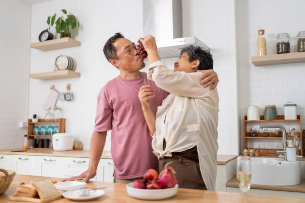 istock Mature asian Couples playfully tease each other with grapes in kitchen. 1958996332