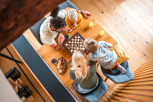 Elevated view on two brothers and their family find delight in a chess game, creating memorable moments and shared laughter at home.
