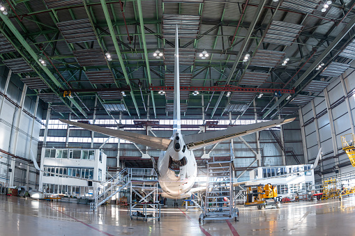 Rear view of a white passenger jetliner in the aviation hangar. Aircraft under maintenance. Checking mechanical systems for flight operations