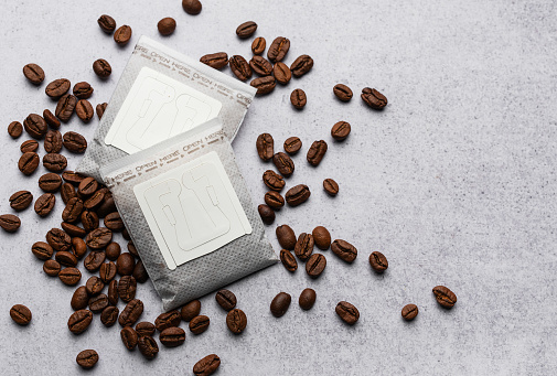 Drip coffee paper bags with coffee beans on a grey concrete background