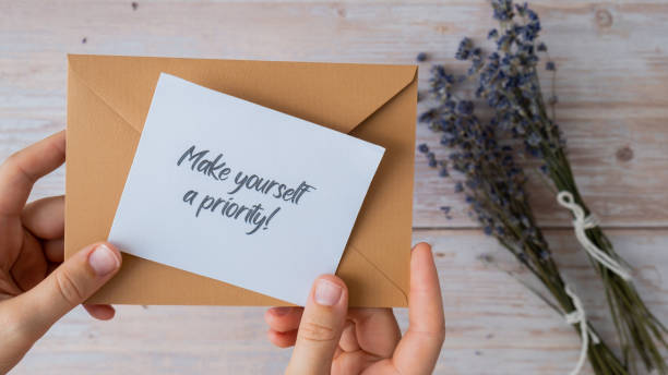 istock Female hands taking paper card note with text MAKE YOURSELF A PRIORITY from beige envelope. Lavender flower. Top view, flat lay. Concept of mental spiritual health self care wellbeing 1959195439