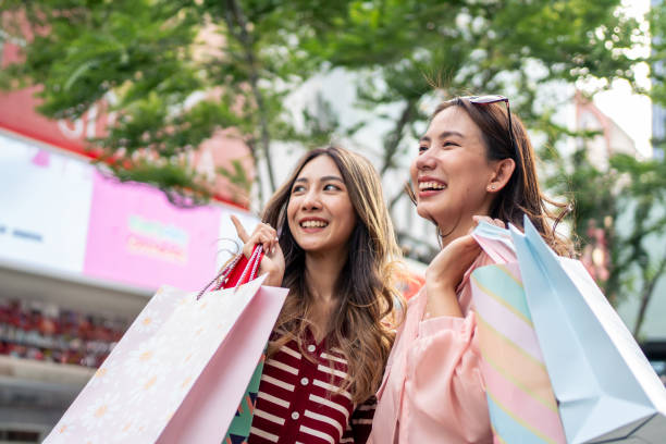 asian young women shopping goods outdoor in shopping street at night. attractive young female friends holding shopping bags then walking with happiness enjoy purchasing in department store together. - two party system ストックフォトと画像