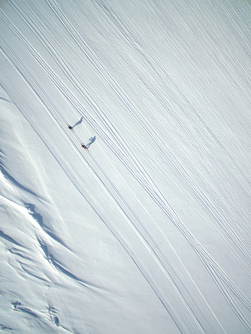 Skiers from above, near Sisimiut, Greenland, Denmark. They cast their shadows onto the snow. This image was taken with a drone.