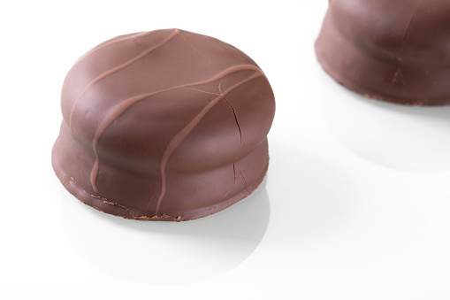 A close-up shot of a shiny, delicious chocolate-coated marshmallow reflecting on a white mirrored surface. The glossy texture creates an enticing visual display.