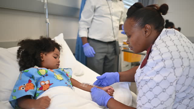 Friendly African nurse putting an IV drip in arm of Cute girl in a hospital bed in a ward with high five
