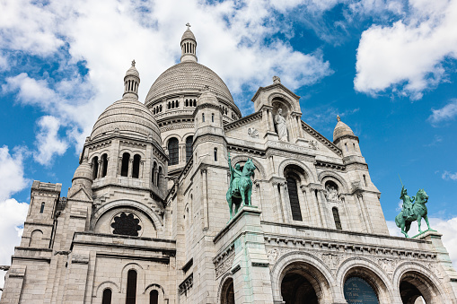 Basilique du Sacre Coeur with equestrian statues on Montmartre in Paris, France, low angle view and cloudy blue sky above