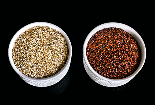 Red and white quinoa on the two white plates on the black background. Healthy food and nutrition concept. Safe, ecological, and healthy products.