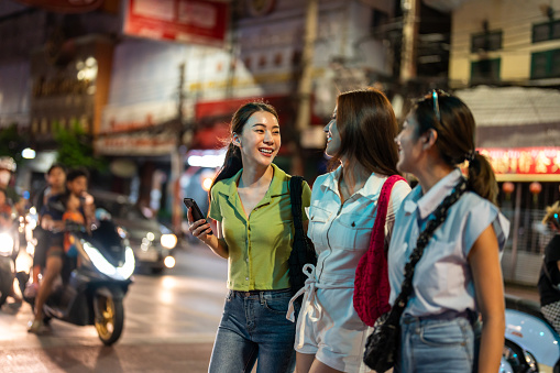 Asian beautiful women friend traveling outdoors in the city at night. Attractive girls tourist feeling happy and relax, walking on street enjoy spend free leisure time for holiday vacation together.