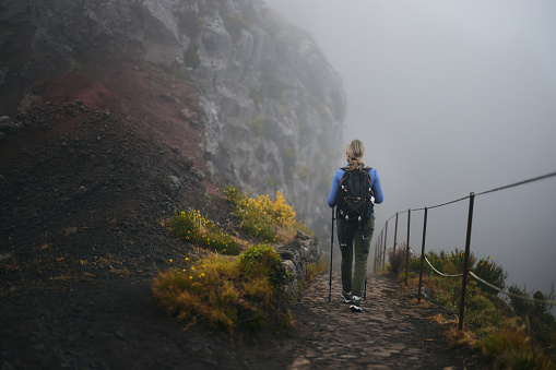 Rear view of carefree female backpacker hiking on a path during foggy day on a mountain. Copy space.