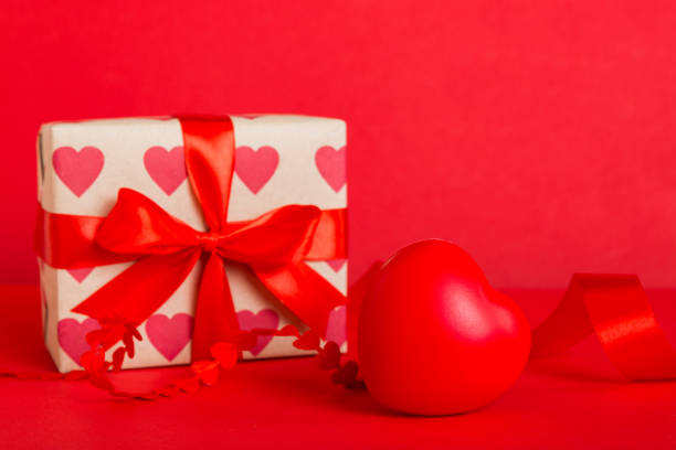 gift box with red bow and red heart on colored background. Perspective view. Flat lay.