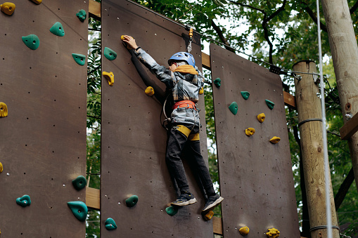 teenage boy climbing up the wall in outdoor adventure park passing obstacle course. high rope park