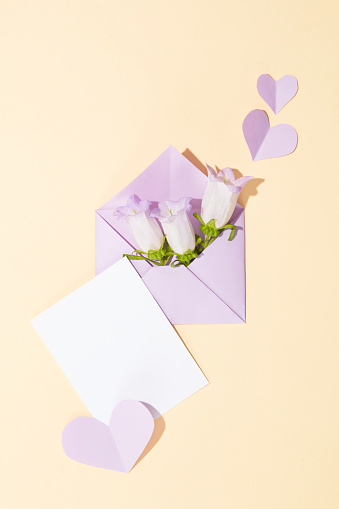 An envelope containing some fresh flowers displayed with handmade paper hearts and a piece of paper with copy space. Copy space for International Women's Day content. Beige background