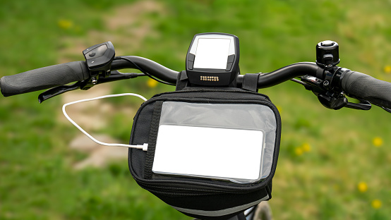E bike handlebars with display and handlebar bag against a green blurred background. Copy space for display and cell phone.