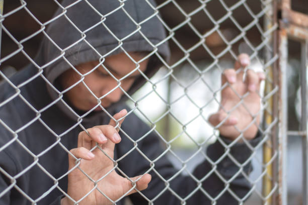 Detented preteens Asian preteen in black hoodie shirt looks sad and puts his hands on metal fence panels around detention building because he was detained for inappropriate behavior, freedom and detention concept. child crimes stock pictures, royalty-free photos & images