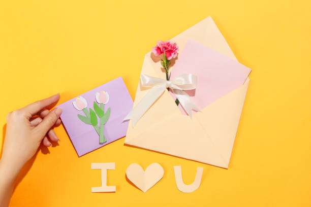 istock A hand next to a card and a pastel pink envelope with a carnation on a yellow background. Copy space with Womens Day theme for advertising. 1959435662